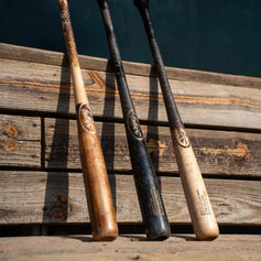 Three game-used Tater pro maple wood bats with worn pine tar finishes leaning against weathered wood boards