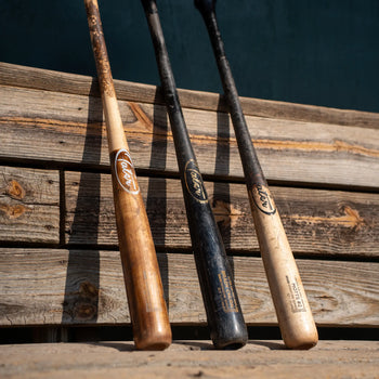Three game-used Tater pro maple wood bats with worn pine tar finishes leaning against weathered wood boards