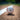A white baseball with red stitching and a black stylized 'PB' logo, resting on a dirt baseball field near a white foul line.