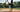 Two-tone Tater maple wood bat leaning against a batting cage net on a baseball field