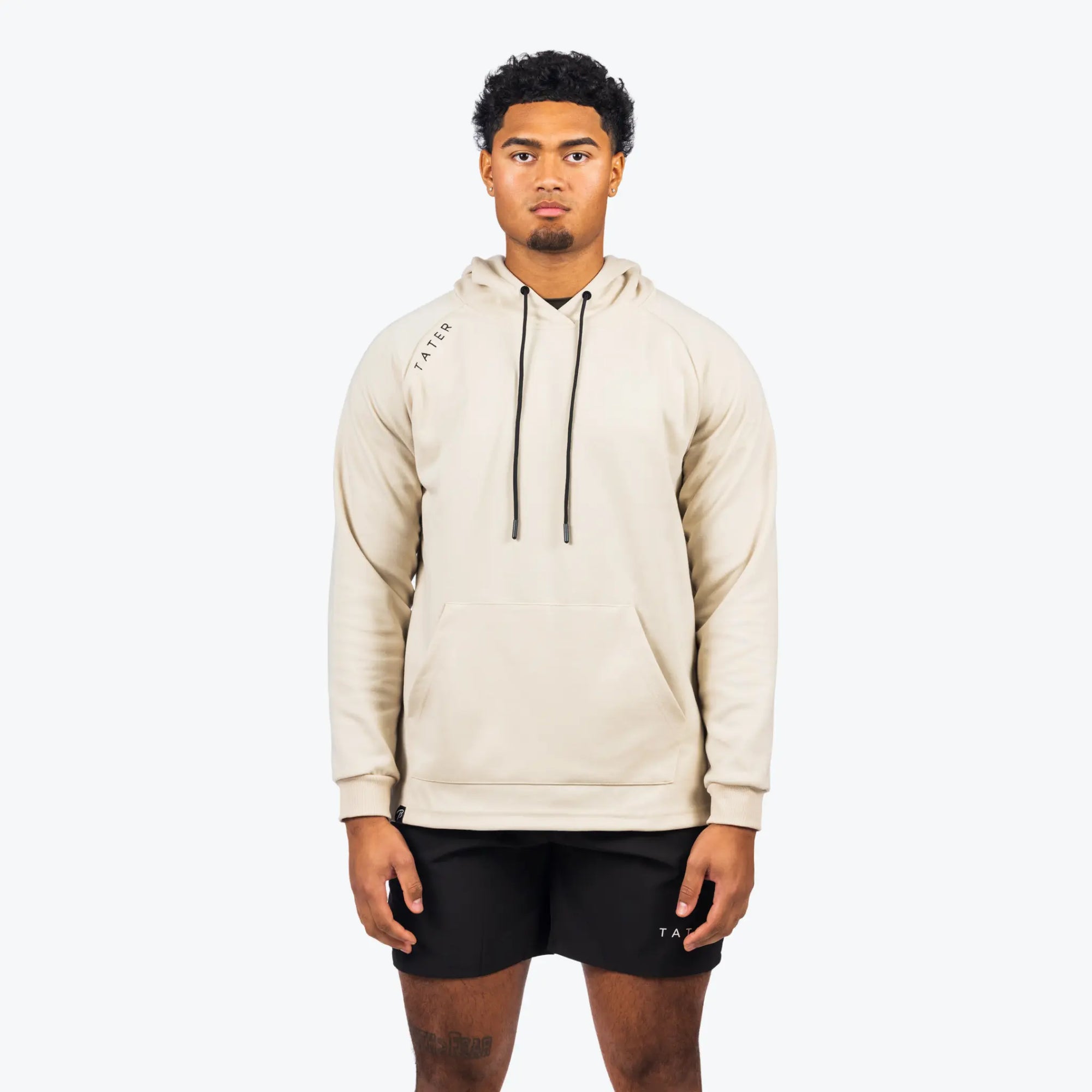 The uploaded image displays a cream-colored, professional baseball training hoodie from the Tater brand. It has long sleeves and features a minimalist design with the "TATER" logo neatly placed on the left chest area. The hoodie appears to be crafted for both athletic functionality and casual athleisure wear, embodying a sleek and straightforward style.