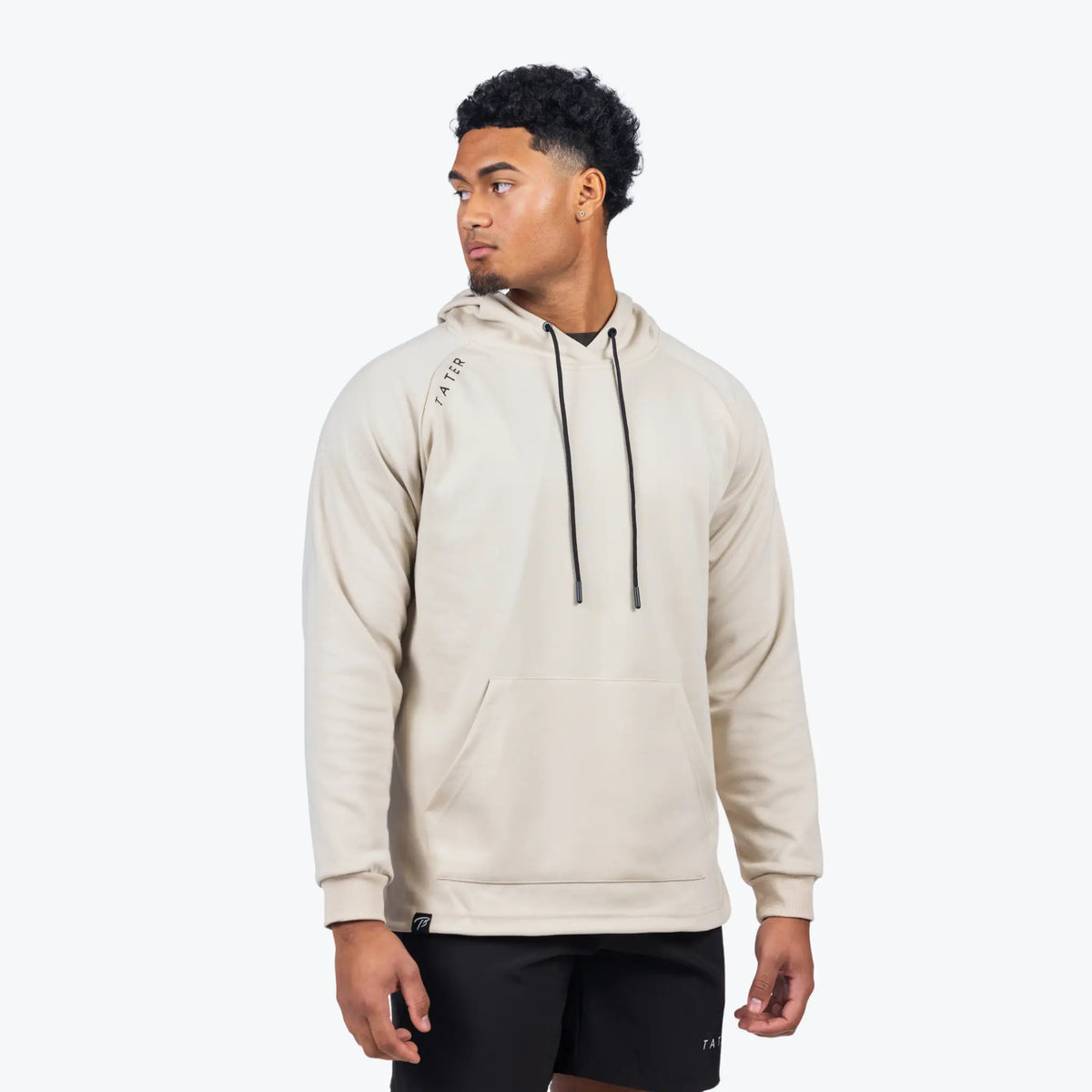 The image features a model in a cream hoodie and black shorts by TATER, suitable for sports or casual wear. The design is minimalist and modern.