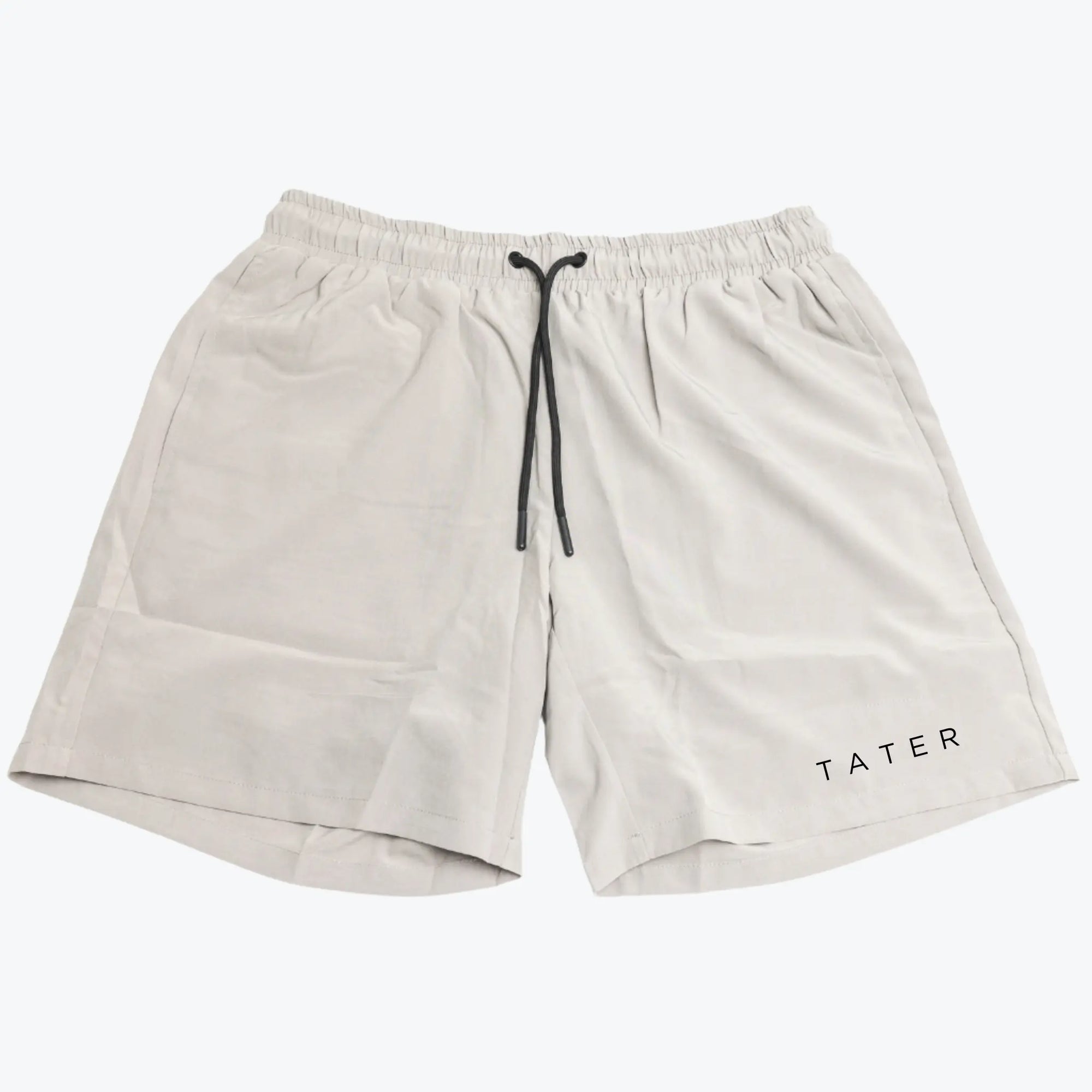 The image features a pair of light grey athletic shorts with a drawstring at the waist. On one leg, the word "TATER" is printed in black, which is the branding of the product. The shorts appear to be designed for physical activity, such as working out or sports practice, given the comfortable and breathable design. The color and minimal branding suggest a versatile piece of athletic wear that could be easily coordinated with other workout gear.