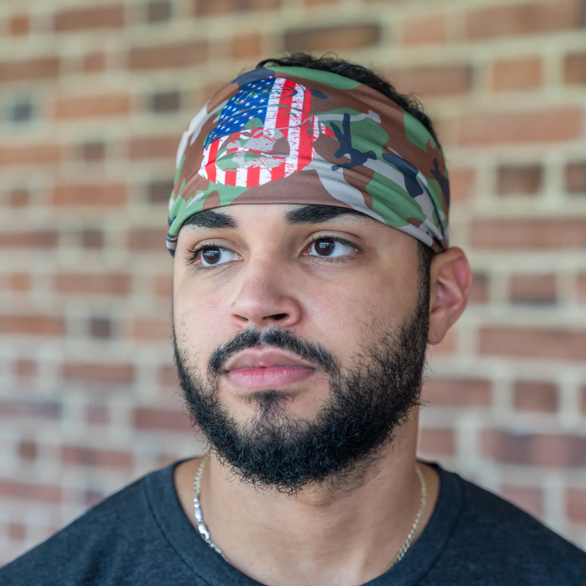 Focused baseball player wearing Tater Baseball&#39;s camo workout headband adorned with the American flag, blending athletic function with national pride in a casual setting.