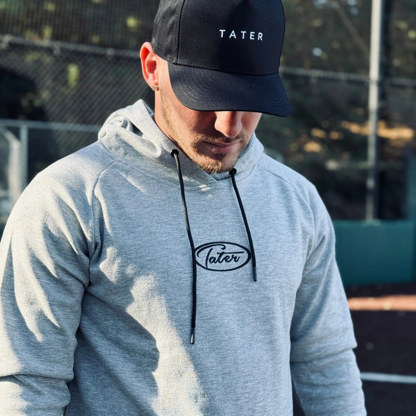 Focused athlete in Tater Baseball gear, wearing a casual grey hoodie with the Tater logo and a sleek black Tater cap, ready for a workout or practice session on the field.
