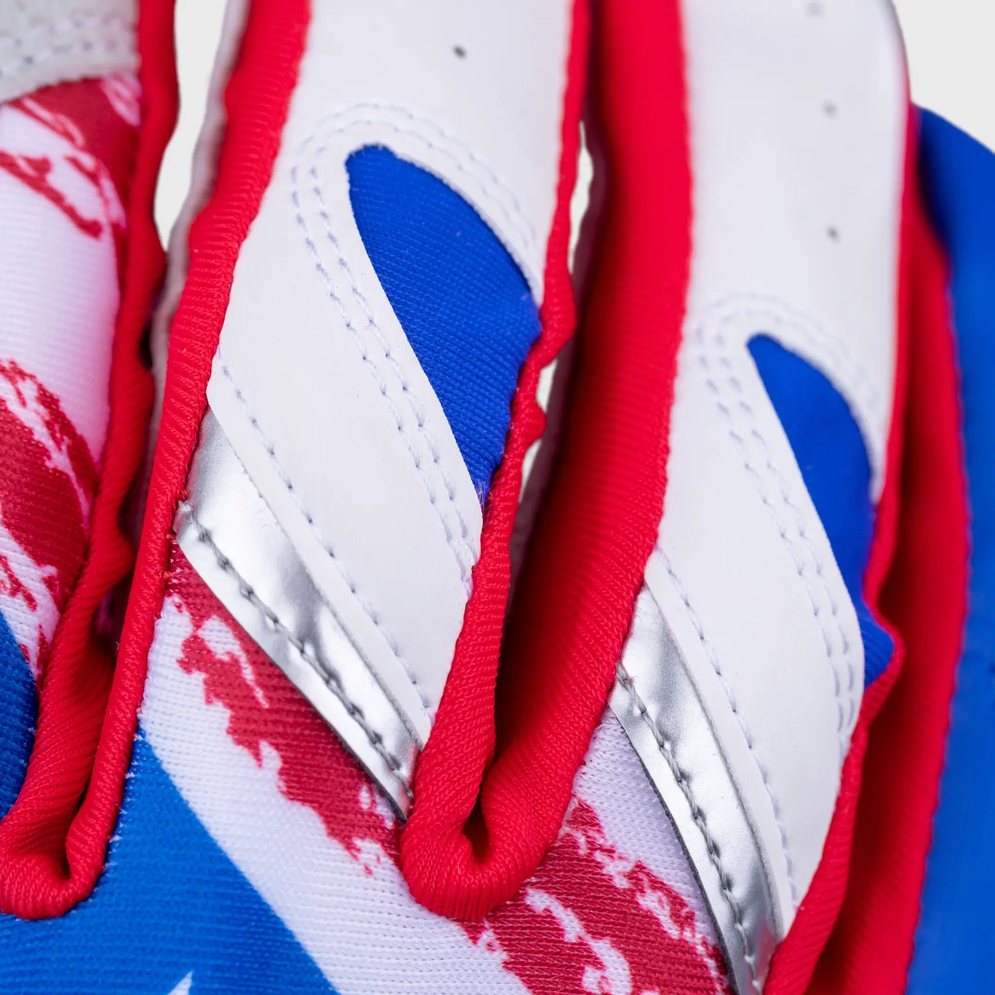 Intimate close-up of Tater Baseball batting gloves displaying the intricate finger design with vibrant red laces against a backdrop of the Puerto Rican flag's colors and pattern