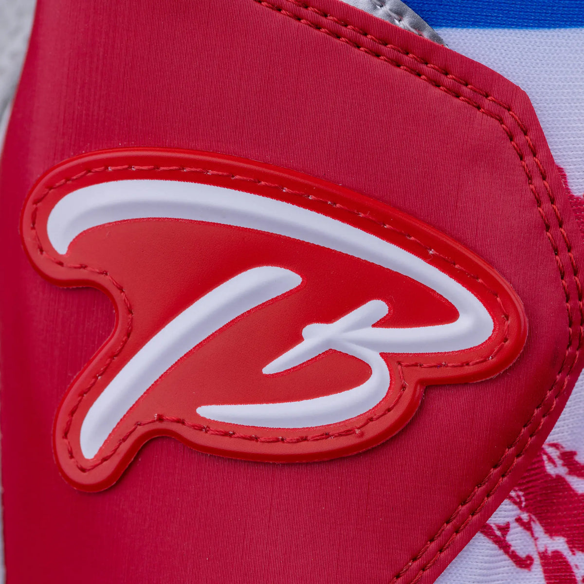 Close-up of the embossed &#39;TB&#39; logo on red leather, part of Tater Baseball&#39;s premium batting gloves with a design inspired by the Puerto Rican flag.