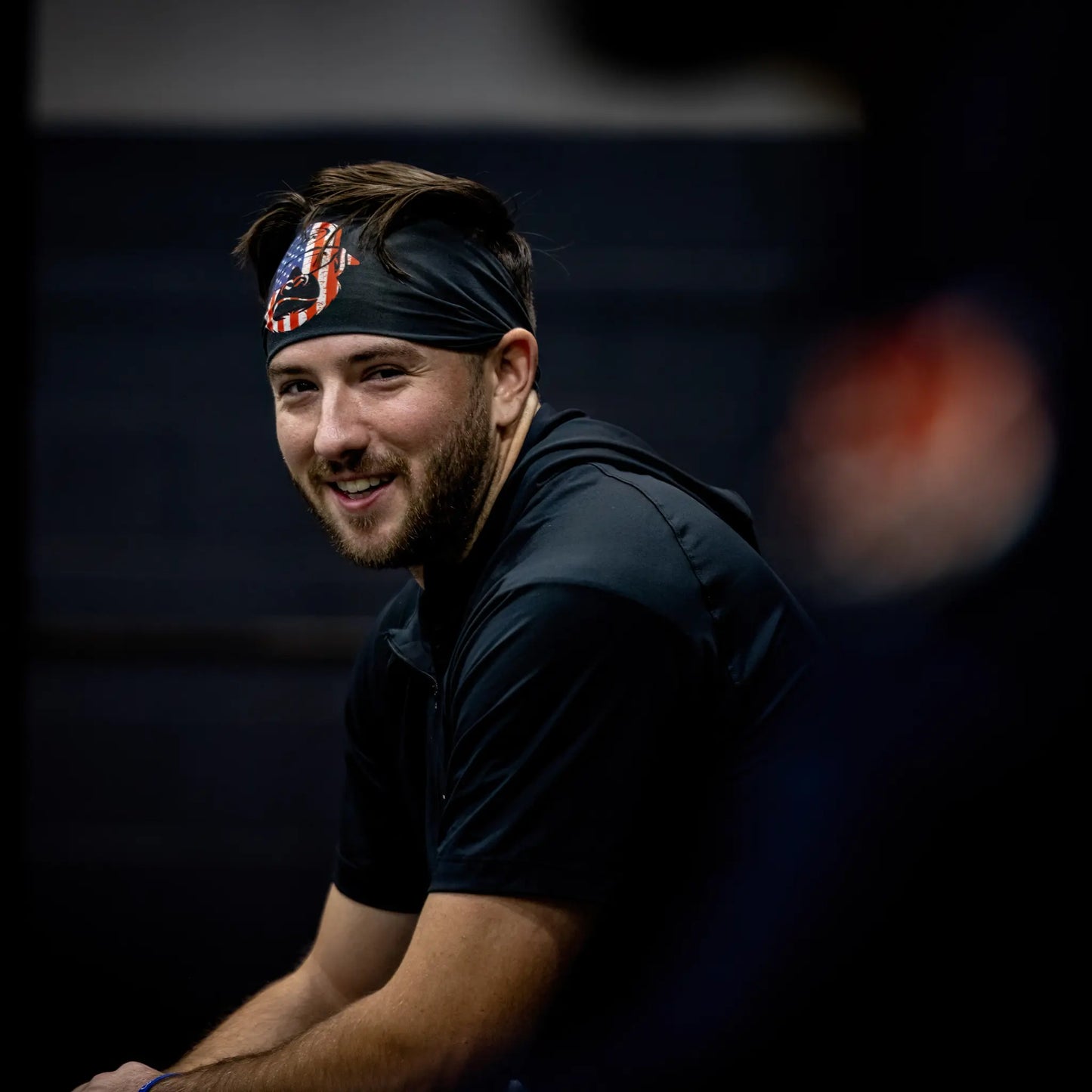 Smiling athlete wearing Tater Baseball's black headband with a bold USA flag Kong design, providing both performance and patriotic style during training.