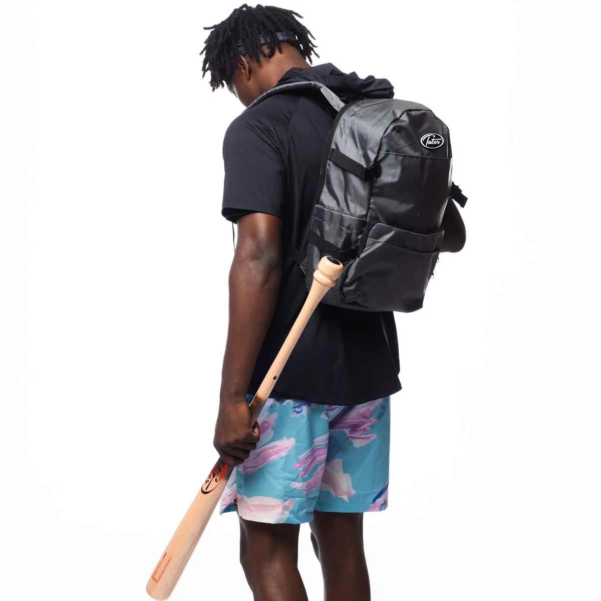 In the photo, an athlete is ready for action with a Tater Baseball backpack and a bat, wearing a black hoodie and eye-catching blue and pink workout shorts. This gear represents Tater Baseball&#39;s blend of style and functionality for the sport.
