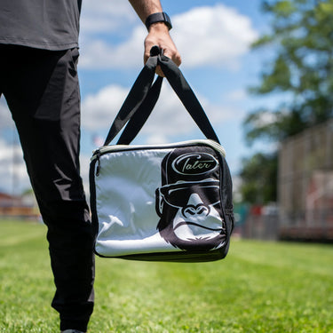 Clear Tater Kong ball bag with black straps carried on a baseball field
