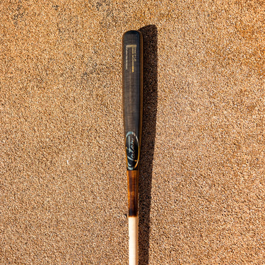 Tater X6 Pro maple bat with a black barrel and natural handle lying on sand